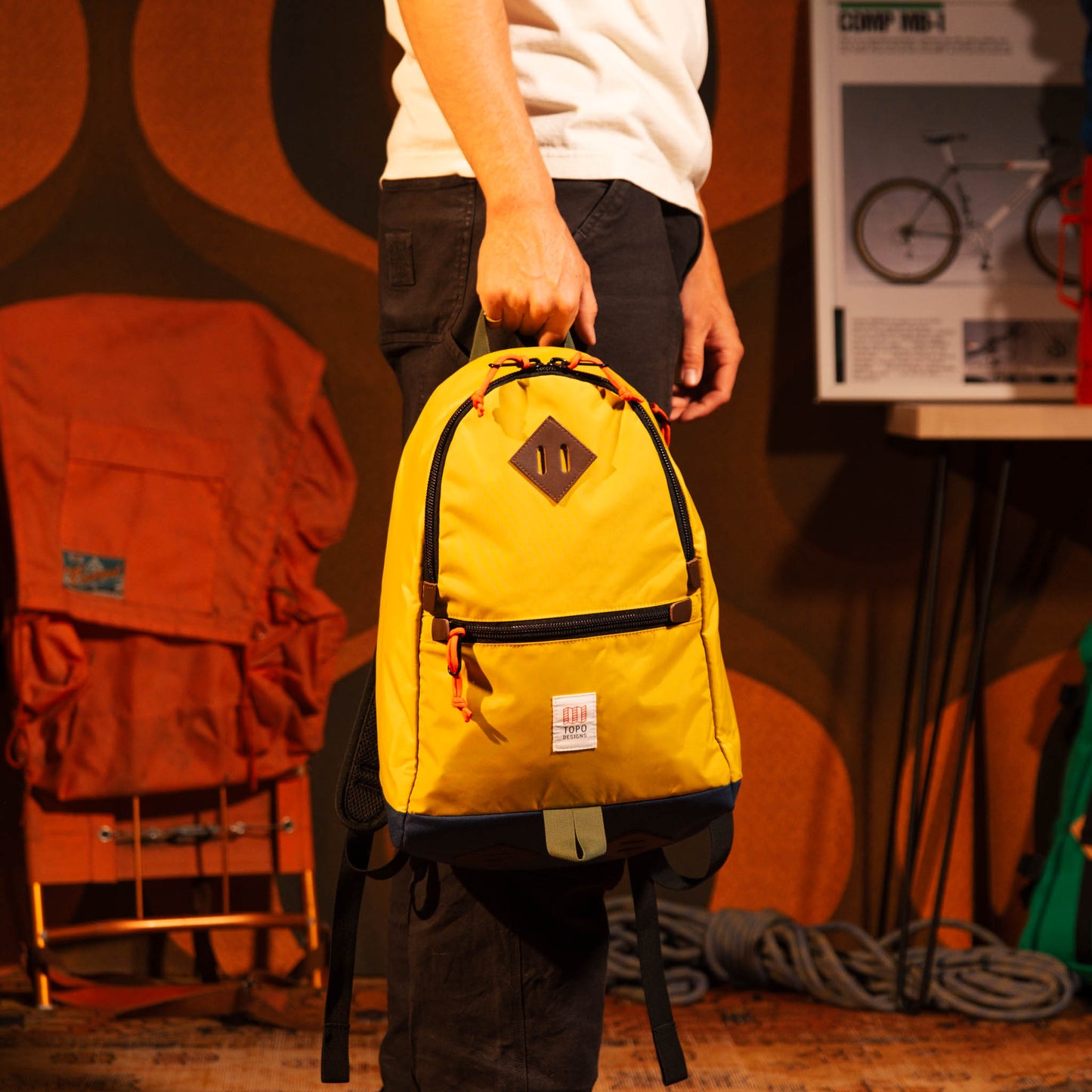General model view of Topo Designs Classic Teardrop Backpack in "Sunset / Midnight" being held by top handle.