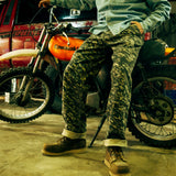 General image of a man wearing camouflage utility pants and brown boots sitting on a Kawasaki motorcycle in front of a red truck.