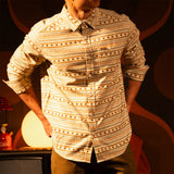 General lifestyle image of person wearing a "Bone White Sunset Stripe" Mountain Shirt Lightweight with a dark background with a warm glow in a dimly lit room. [Model is 5'11", wearing size medium]