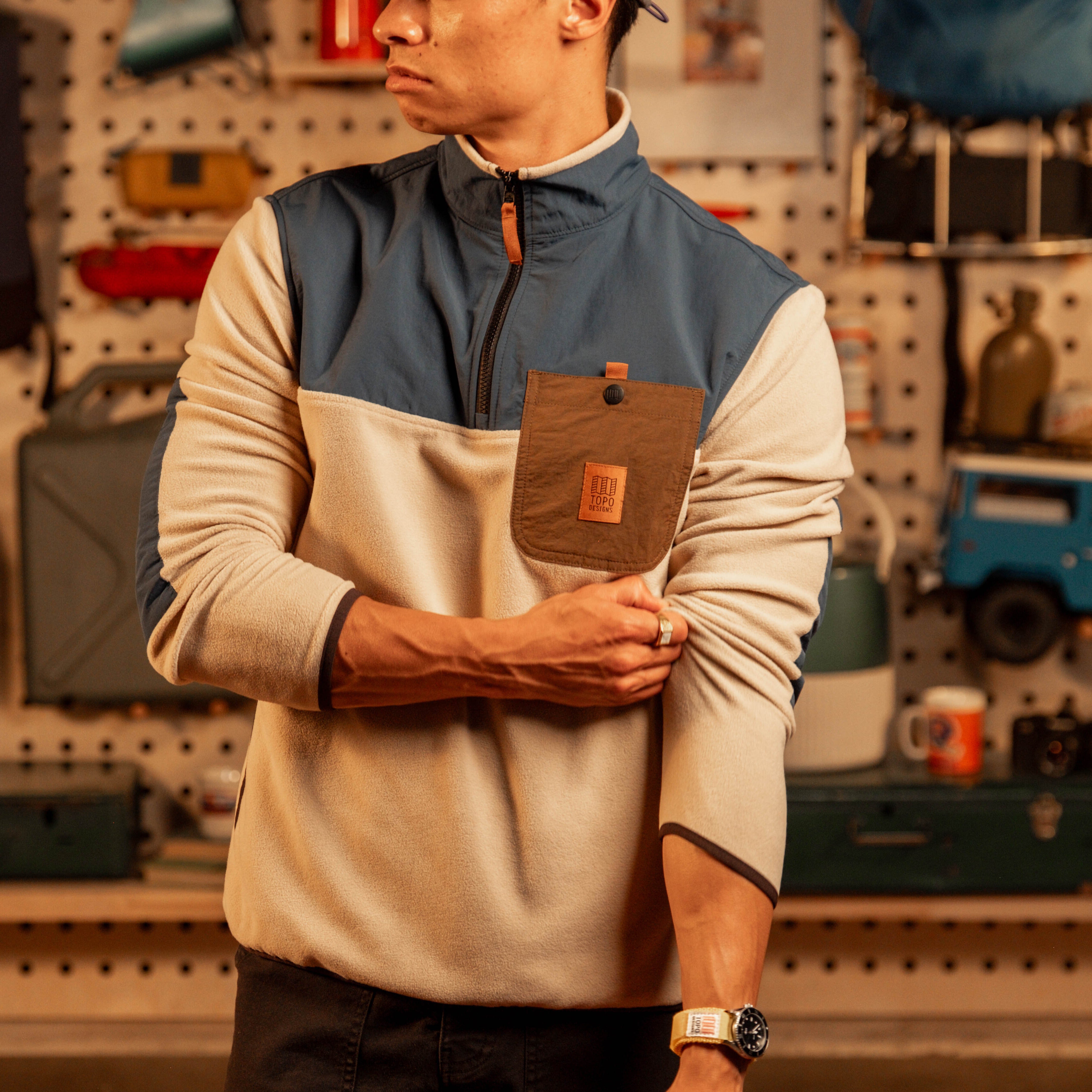 Men's fleece pullover with cream body, navy chest panel, brown pocket detail, and quarter-zip in garage setting. [Model is 5'11", wearing size medium]